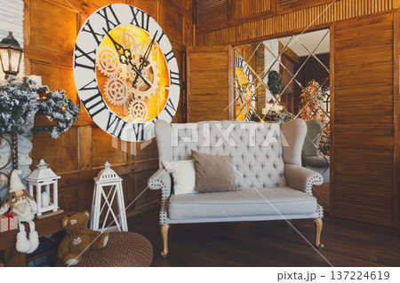 Beautiful holdiay living room. Big magical clock on wooden wall and soft cozy gray couch. Winter holiday design and decorations background Beautiful holdiay living room. Big magical clock on wooden wall and soft cozy gray couch. Winter holiday design and decorations background 137224619
