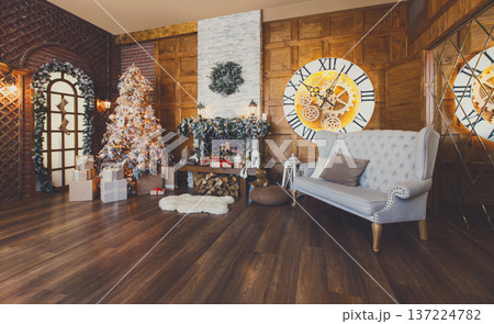 Beautiful christmas interior. Warm room with fireplace, decorated christmas tree, lots of presents and huge clock on wooden wall. Cozy home for winter holidays, copy space 137224782