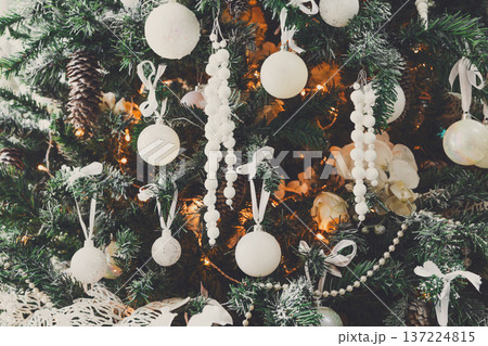 Winter holidays atmosphere background. Closeup of beautifully decorated fir tree with modern white baubles, beards and shiny garland. Christmas and new year magic at home 137224815