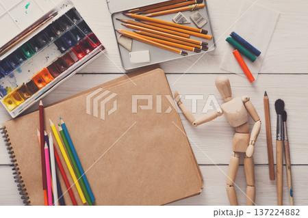 Artist workspace. Paints, sketchbook and wooden painter man with brushes on white desk, top view, flat lay, objects 137224882