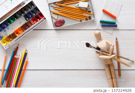Drawing tools, stationary supplies, workplace of artist. Paints and wooden painter man with brushes on white desk, top view, flat lay, objects 137224926