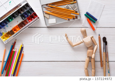 Drawing tools, stationary supplies, workplace of artist. Paints and wooden painter man with brushes on white desk, top view, flat lay, objects 137224972