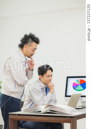 会社で資料を見ながら打ち合わせするエンジニア　 137225120