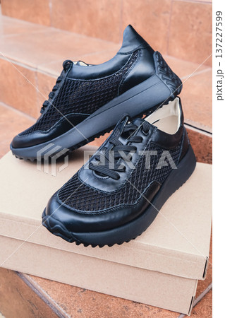 Elegant black leather womens shoes blank product for branding displayed on recycled cardboard box. New casual female sneakers no-brand footwear e-commerce. No logo product 137227599
