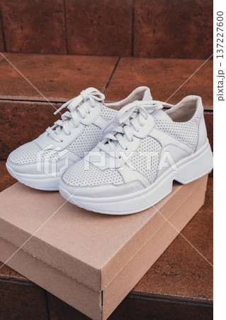 Minimalist eco-friendly white sneakers placed on recycled cardboard box, clean design for sustainable fashion concepts. New unbranded white sneakers footwear mockups and modern product displays. For 137227600
