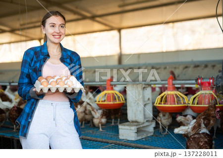 Smiling woman standing in henhouse with cardboard tray of eggs Smiling woman standing in henhouse with cardboard tray of eggs 137228011