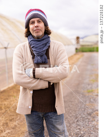 Middle-aged man standing on rural path near greenhouses Middle-aged man standing on rural path near greenhouses 137228182
