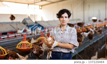 young Latin woman farmer worker in gloves taking care of chicken during work in henhouse, indoors 137228464