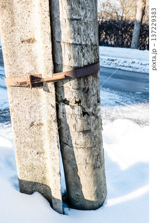 Broken Wooden Utility Pole Secured To Concrete Post With Metal Clamp In Winter 137229383