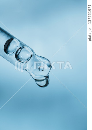Glass pipette dropper collecting blue liquid drop on light blue background Glass pipette dropper collecting blue liquid drop on light blue background 137231971