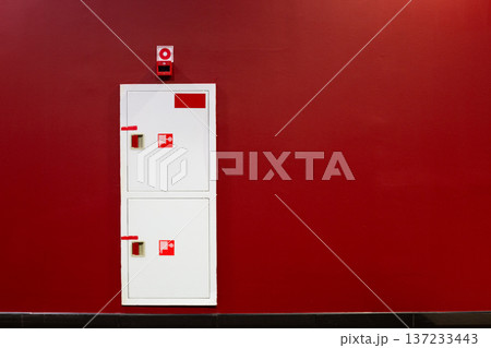 Fire boxes in red wall. Safety element hidden in the wall for timely fire extinguishing. Building safety thanks to water hose located in wall. Building fire concept with space for text Fire boxes in red wall. Safety element hidden in the wall for timely fire extinguishing. Building safety thanks to water hose located in wall. Building fire concept with space for text 137233443