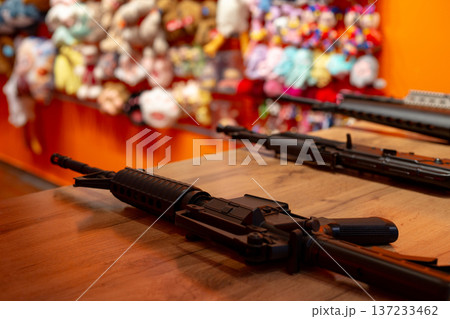 Gun on shooting range table with toy backdrop to win by shooting at target. Participate in shooting range to test your luck and win stuffed animal prize. Win gift using rifle. Romantic shooting range Gun on shooting range table with toy backdrop to win by shooting at target. Participate in shooting range to test your luck and win stuffed animal prize. Win gift using rifle. Romantic shooting range 137233462