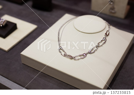 Silver chain necklace showcased on a white display stand, with other jewelry pieces arranged in the background within a retail environment Silver chain necklace showcased on a white display stand, with other jewelry pieces arranged in the background within a retail environment 137233815