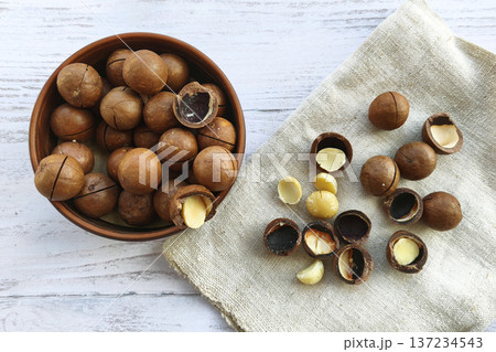 Macadamia nuts in shells with cracked kernels in a bowl on a rustic table. Healthy snack, organic food, and natural nutrition Macadamia nuts in shells with cracked kernels in a bowl on a rustic table. Healthy snack, organic food, and natural nutrition 137234543