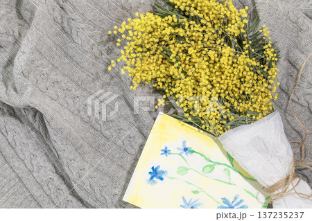 Yellow Mimosa Bouquet Wrapped In Paper With Kid Picture On Gray Knitted Background Yellow Mimosa Bouquet Wrapped In Paper With Kid Picture On Gray Knitted Background 137235237