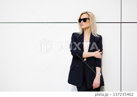 Portrait of sexy stylish woman standing in the street in black suit, wearing sunglasses on sunny spring day Portrait of sexy stylish woman standing in the street in black suit, wearing sunglasses on sunny spring day 137235462