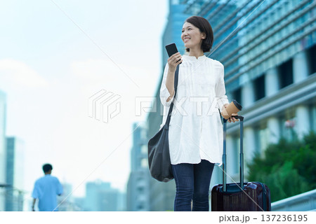 街中でスーツケースとスマートフォンを持つ女性 街中でスーツケースとスマートフォンを持つ女性 137236195
