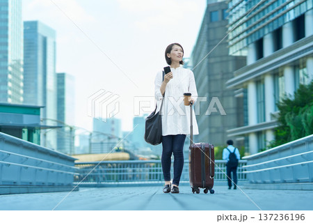 街中でスーツケースとスマートフォンを持つ女性 137236196