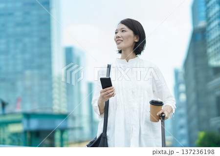 街中でスーツケースとスマートフォンを持つ女性 街中でスーツケースとスマートフォンを持つ女性 137236198