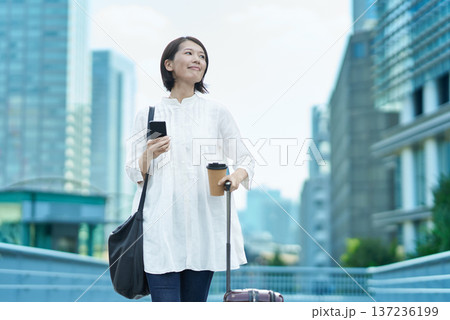 街中でスーツケースとスマートフォンを持つ女性 街中でスーツケースとスマートフォンを持つ女性 137236199