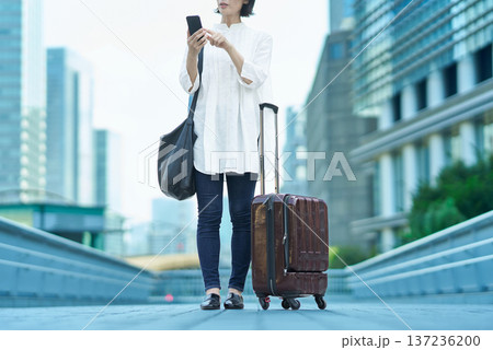 街中でスーツケースとスマートフォンを持つ女性 街中でスーツケースとスマートフォンを持つ女性 137236200