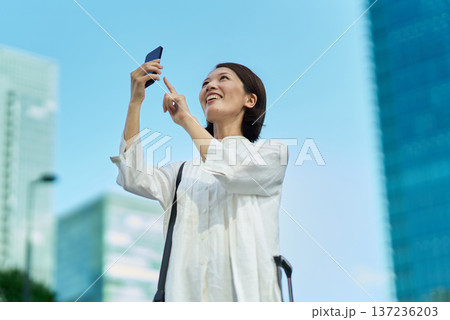 街中でスーツケースとスマートフォンを持つ女性 137236203