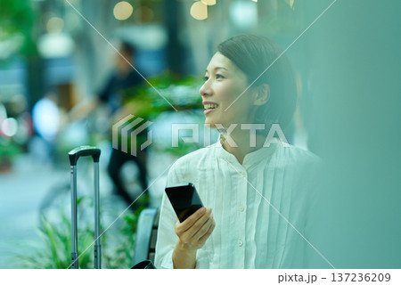 街中でスーツケースとスマートフォンを持つ女性 137236209
