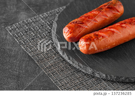 Grilled sausages fried two, on slate stone plate round, dark background, selective focus  137236285
