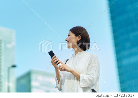 晴れた日の街なかでスマートフォンを掲げる女性 晴れた日の街なかでスマートフォンを掲げる女性 137238017