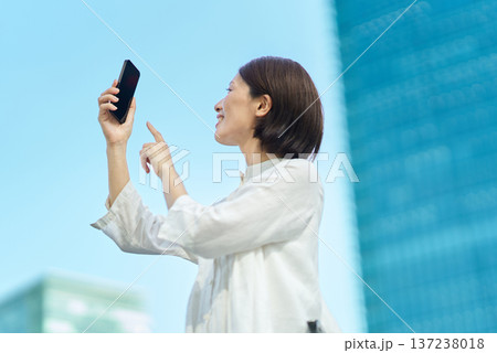 晴れた日の街なかでスマートフォンを掲げる女性 137238018