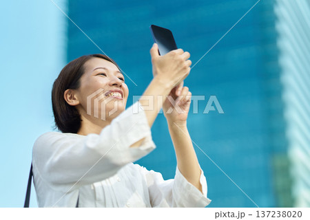 晴れた日の街なかでスマートフォンを掲げる女性 晴れた日の街なかでスマートフォンを掲げる女性 137238020