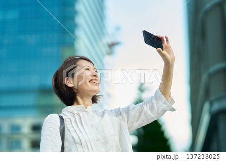 晴れた日の街なかでスマートフォンを掲げる女性 晴れた日の街なかでスマートフォンを掲げる女性 137238025