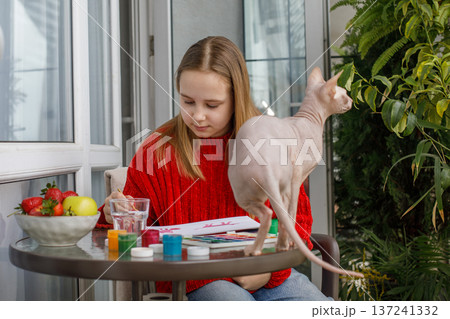 Attractive child girl painting and sitting with cat pet on the terrace. Kid 11 years old 137241332