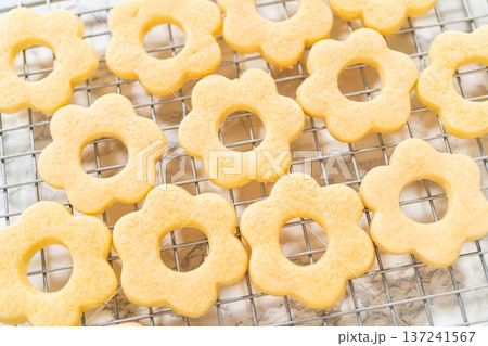 Brightly lit flower cookies sit cooling on a metal rack, made for the Easter Cookie Sandwich with Raspberry Buttercream. Perfect for festive spring decorating. 137241567
