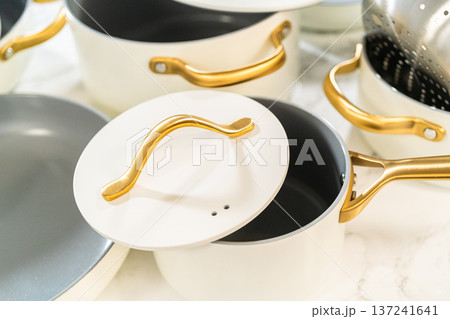 A close-up shot of a white cookware set featuring ceramic pots with gold handles and matching lids. Suitable for editorial kitchen content or product showcases. 137241641