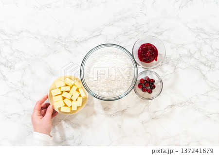 The ingredients for cranberry buttercream are laid out, including cubes of butter, powdered sugar, cranberry sauce, and fresh cranberries. 137241679