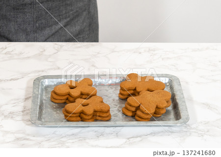 Gingerbread cookies, including a gingerbread man with a heart-shaped cutout, rest on a rustic metal tray against a marble countertop. Gingerbread cookies, including a gingerbread man with a heart-shaped cutout, rest on a rustic metal tray against a marble countertop. 137241680