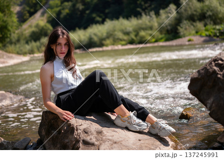 Relaxed Young Woman Resting on Rocks by a Mountain River 137245991