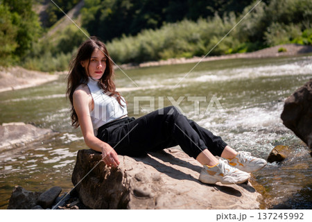 Relaxed Young Woman Resting on Rocks by a Mountain River 137245992