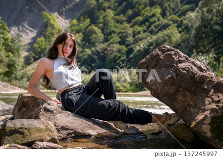 Relaxed Young Woman Resting on Rocks by a Mountain River 137245997