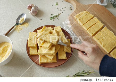Anonymous person places slices of hard polenta on plate. Cornmeal in kitchen. Ingredients and traditional Italian cuisine. Anonymous person places slices of hard polenta on plate. Cornmeal in kitchen. Ingredients and traditional Italian cuisine. 137246233