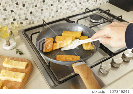 Anonymous person fries pieces of crispy breaded polenta in pan. Cornmeal and chips, snacks in kitchen. Ingredients and traditional Italian cuisine. Anonymous person fries pieces of crispy breaded polenta in pan. Cornmeal and chips, snacks in kitchen. Ingredients and traditional Italian cuisine. 137246241