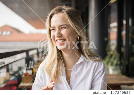 Laughing woman sitting on a cafe terrace enjoying a cheerful conversation. Happiness, friendship, urban social life, communication and joyful everyday moments in the city. 137246627