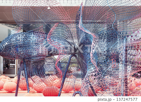 This expansive, abstract sculpture reimagines the Siamese fighting fish through a fluid tapestry of interlocking wire mesh and shimmering reflective discs. The woven steel forms an intricate, organic 137247577