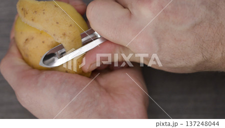 Person peels a potato with a peeler in a kitchen setting during the daytime preparing for cooking Person peels a potato with a peeler in a kitchen setting during the daytime preparing for cooking 137248044