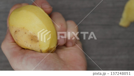 Holding a fresh yellow potato with a hand above a gray surface during a kitchen preparation activity Holding a fresh yellow potato with a hand above a gray surface during a kitchen preparation activity 137248051