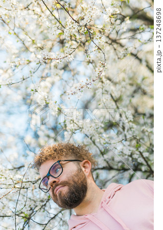 Man standing under flowering tree branches during bright spring bloom. Contemplation, calm lifestyle, connection with nature, seasonal renewal and peaceful outdoor moment in blooming spring garden 137248698