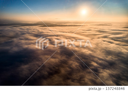 Aerial view of vibrant sunset over white dense clouds bathes in warm golden light, creating dreamlike landscape. Soft shadows play across undulating clouds, while distant landforms peek through mist. Aerial view of vibrant sunset over white dense clouds bathes in warm golden light, creating dreamlike landscape. Soft shadows play across undulating clouds, while distant landforms peek through mist. 137248846