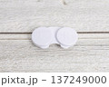 木目背景に置かれた白いコンタクトケース 137249000