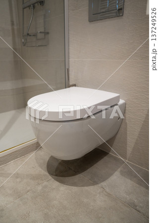 Modern bathroom interior showing a clean white wall-hung toilet with a closed lid, integrated into contemporary tiled decor, focusing on hygiene, luxury, and design Modern bathroom interior showing a clean white wall-hung toilet with a closed lid, integrated into contemporary tiled decor, focusing on hygiene, luxury, and design 137249526